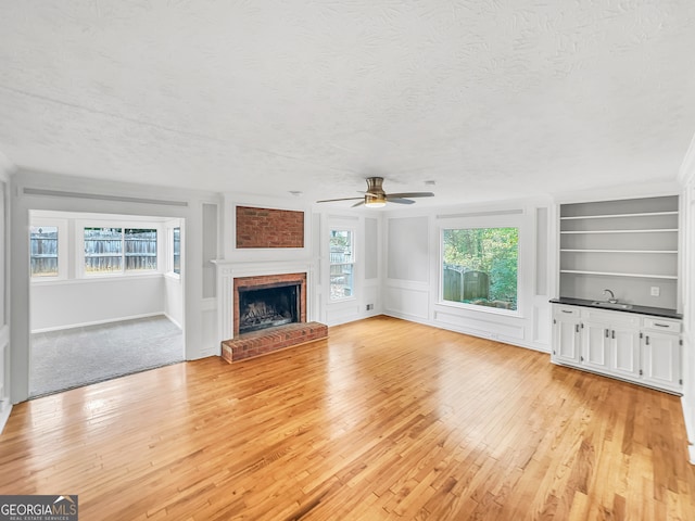 unfurnished living room with light wood-type flooring, a textured ceiling, ceiling fan, and a brick fireplace