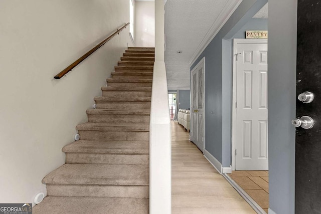 stairs with wood-type flooring, a textured ceiling, and ornamental molding