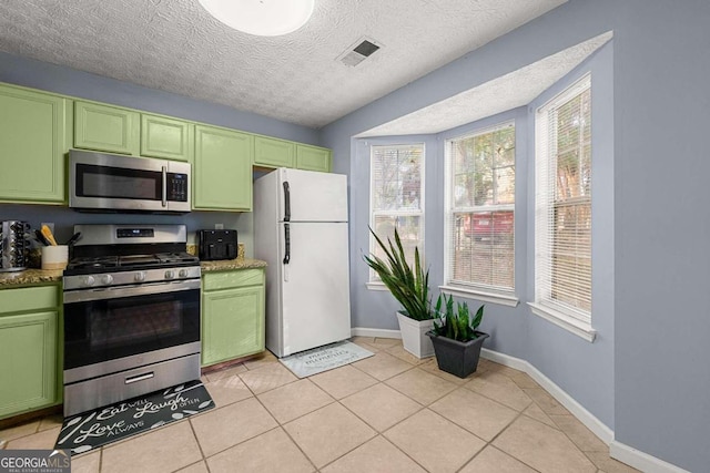 kitchen featuring green cabinets, stainless steel appliances, a textured ceiling, and light tile patterned floors