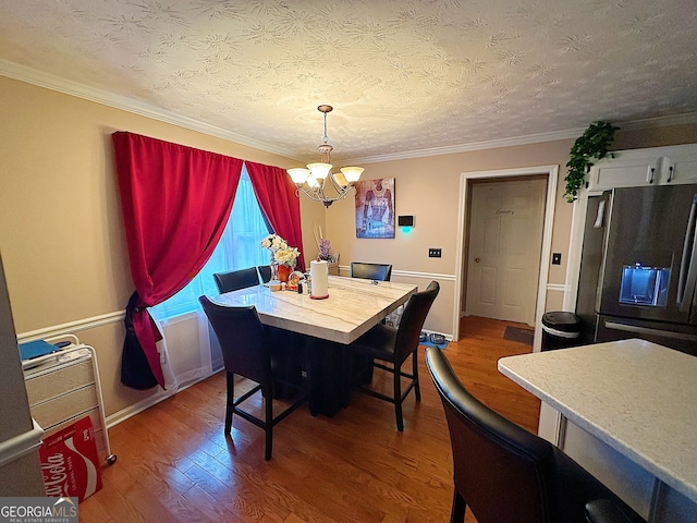 dining space with a textured ceiling, hardwood / wood-style flooring, ornamental molding, and a notable chandelier