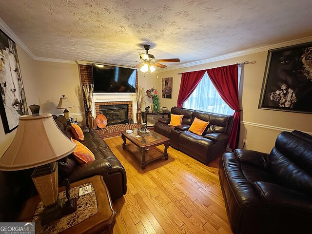 living room with a brick fireplace, light hardwood / wood-style floors, a textured ceiling, ornamental molding, and ceiling fan