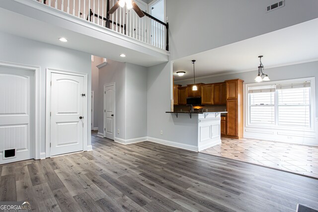 unfurnished living room featuring crown molding, ceiling fan with notable chandelier, hardwood / wood-style flooring, and a high ceiling