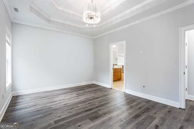 empty room with dark wood-type flooring, a raised ceiling, crown molding, and a notable chandelier