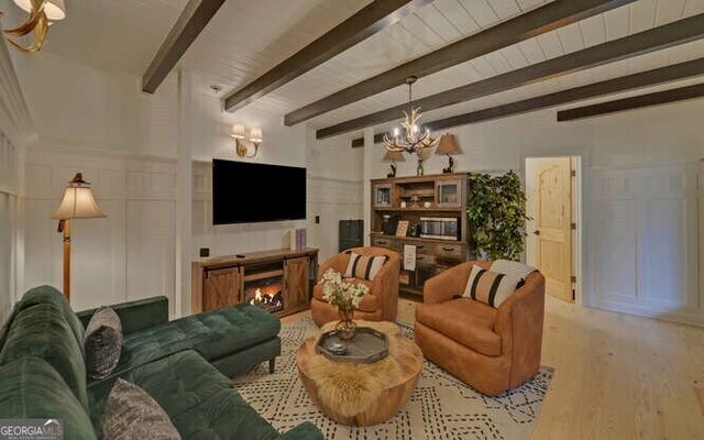 7670 Hiawassee Wilderness Trl, Hiawassee, GA 30546 - living area with a chandelier, a decorative wall, wood finished floors, beamed ceiling, and a lit fireplace