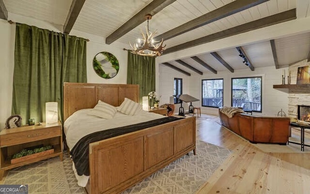 bedroom featuring a stone fireplace, a chandelier, light hardwood / wood-style flooring, and vaulted ceiling with beams