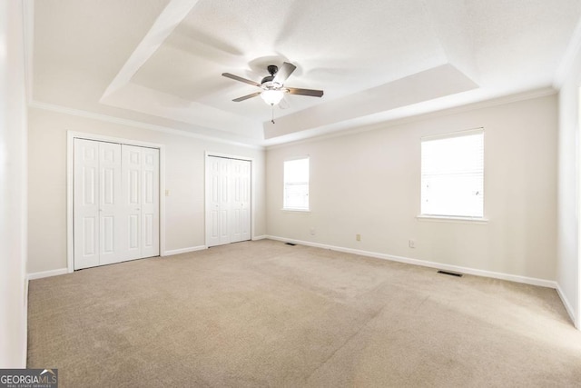 unfurnished bedroom featuring two closets, a tray ceiling, ceiling fan, and light colored carpet