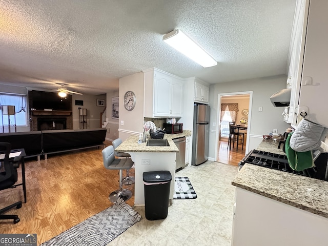 kitchen with a brick fireplace, a kitchen breakfast bar, white cabinets, stainless steel appliances, and light stone counters