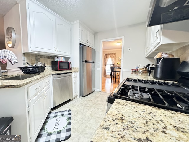 kitchen featuring appliances with stainless steel finishes, white cabinetry, tasteful backsplash, sink, and ventilation hood