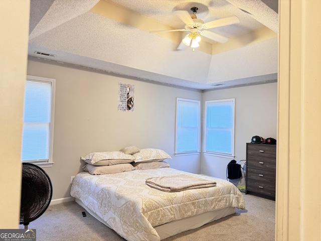 bedroom with light colored carpet, a textured ceiling, a tray ceiling, and ceiling fan