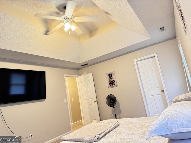 bedroom featuring ceiling fan, a textured ceiling, and a tray ceiling