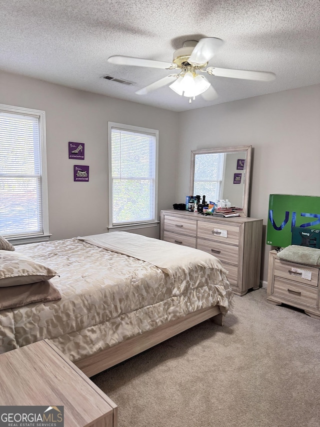 bedroom featuring ceiling fan, light colored carpet, and a textured ceiling