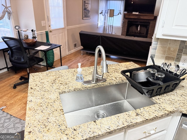 kitchen featuring wood-type flooring, white cabinets, tasteful backsplash, light stone counters, and a fireplace