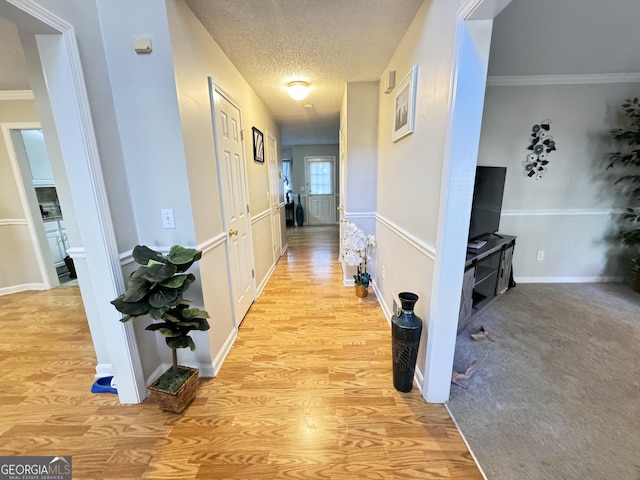 hallway with light wood-type flooring, ornamental molding, and a textured ceiling