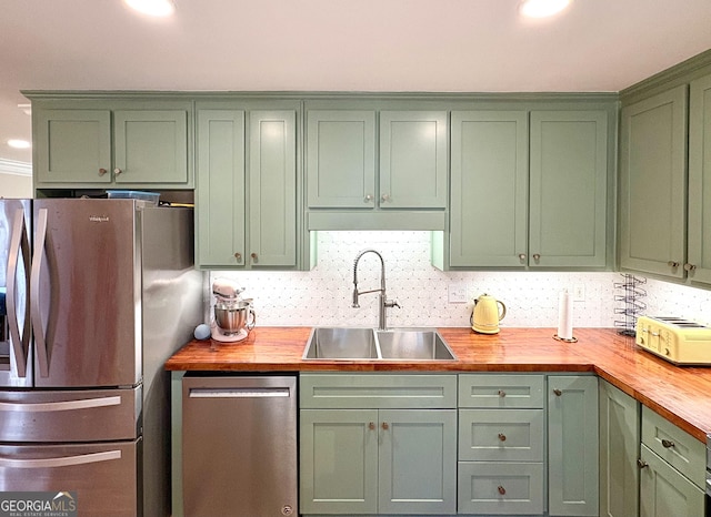 kitchen with appliances with stainless steel finishes, sink, butcher block countertops, green cabinetry, and decorative backsplash