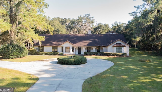 ranch-style house featuring covered porch, a front yard, curved driveway, stucco siding, and a chimney