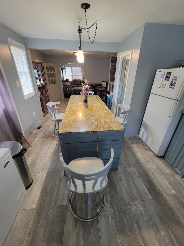 kitchen featuring hanging light fixtures, light stone countertops, wood-type flooring, and white refrigerator