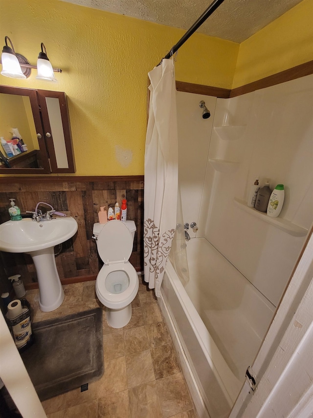 full bathroom featuring a textured ceiling, wood walls, shower / bath combo, sink, and toilet