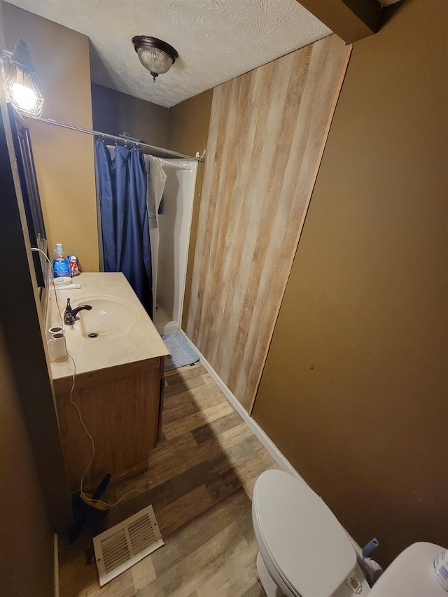 bathroom featuring walk in shower, vanity, a textured ceiling, hardwood / wood-style flooring, and toilet