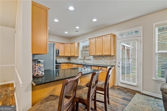 kitchen featuring a kitchen bar, sink, tasteful backsplash, dark hardwood / wood-style floors, and dark stone countertops