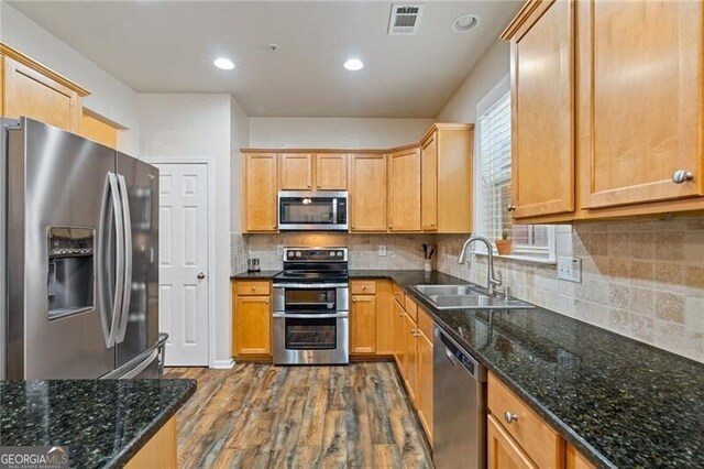 kitchen with stainless steel appliances, wood-type flooring, sink, backsplash, and dark stone countertops