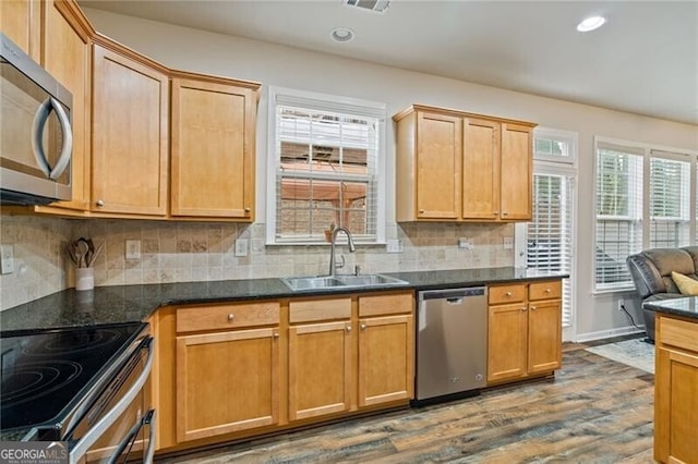 kitchen with sink, decorative backsplash, appliances with stainless steel finishes, dark stone counters, and dark hardwood / wood-style flooring