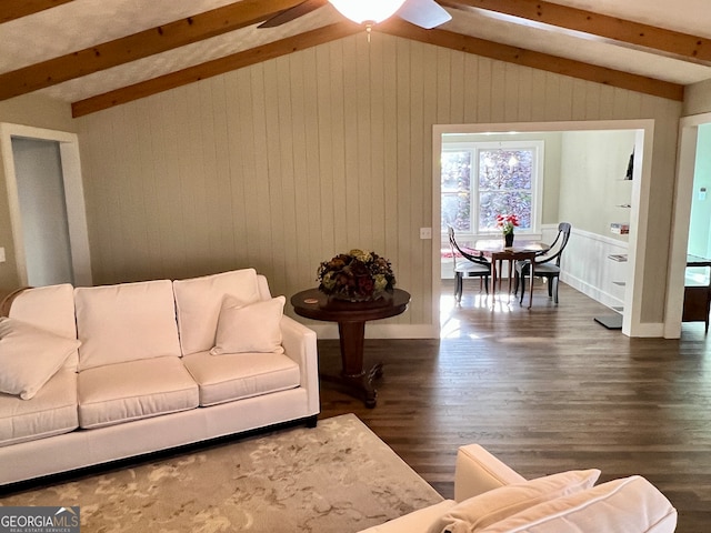 living room featuring lofted ceiling with beams, ceiling fan, dark wood-type flooring, and wood walls