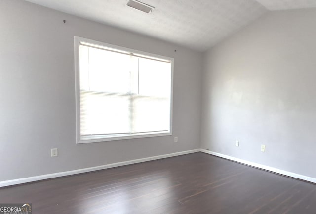 spare room featuring dark hardwood / wood-style flooring, a textured ceiling, and vaulted ceiling