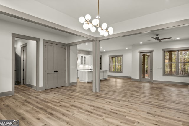 unfurnished living room featuring ceiling fan with notable chandelier, light hardwood / wood-style floors, and plenty of natural light