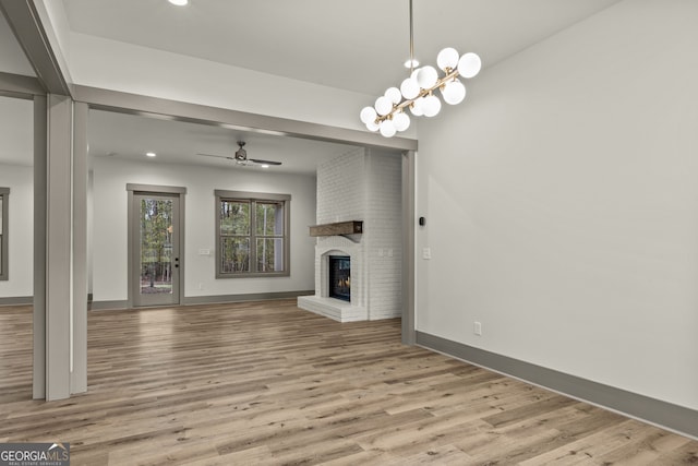 unfurnished living room featuring ceiling fan with notable chandelier, a brick fireplace, and light hardwood / wood-style flooring