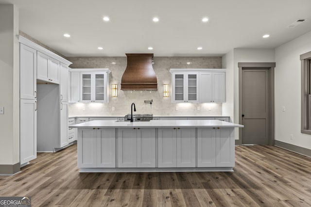 kitchen featuring hardwood / wood-style floors, custom range hood, and a center island with sink