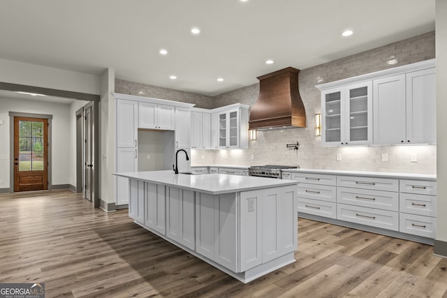 kitchen with white cabinets, light hardwood / wood-style floors, a center island with sink, and custom exhaust hood