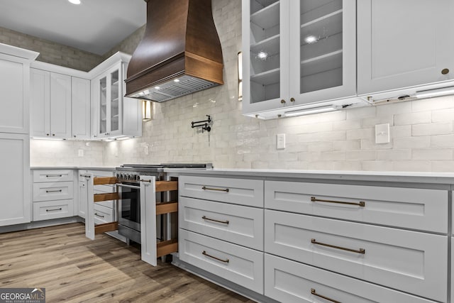 kitchen featuring white cabinets, high end range, tasteful backsplash, custom exhaust hood, and light wood-type flooring