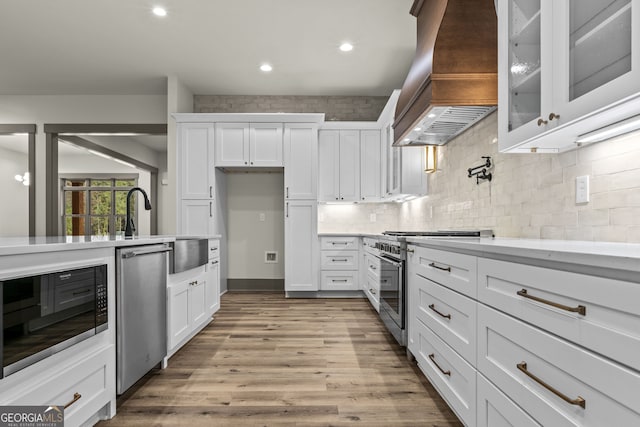 kitchen featuring stainless steel appliances, light hardwood / wood-style floors, decorative backsplash, custom range hood, and white cabinetry