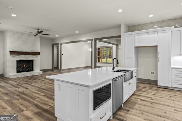 kitchen with black microwave, white cabinetry, sink, and a kitchen island with sink