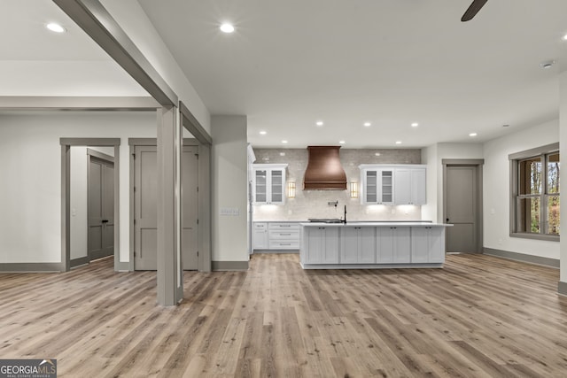 kitchen with a kitchen island with sink, light wood-type flooring, custom range hood, and white cabinets