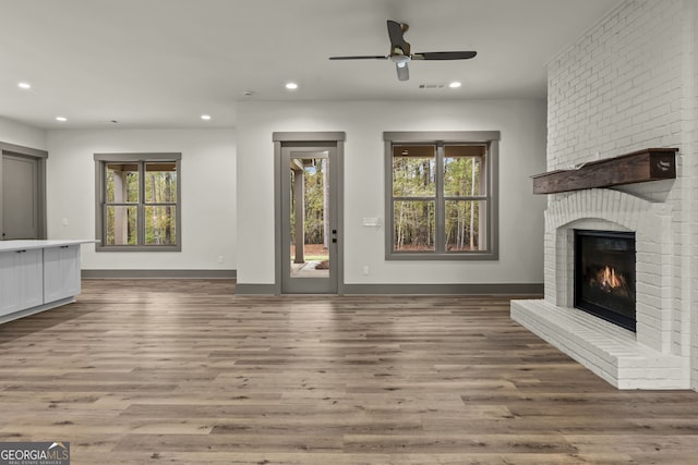 unfurnished living room with a brick fireplace, hardwood / wood-style flooring, and ceiling fan