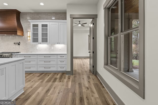 kitchen featuring light hardwood / wood-style flooring, custom exhaust hood, stainless steel stove, and white cabinets