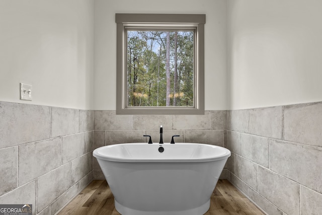 bathroom with tile walls, hardwood / wood-style flooring, and a bathing tub