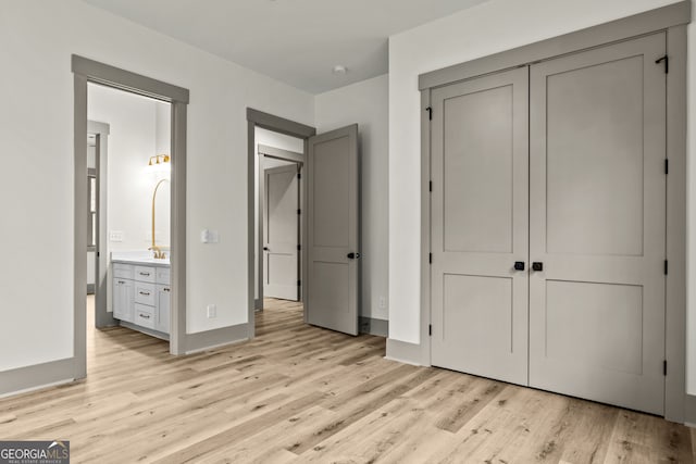 unfurnished bedroom with a closet, light wood-type flooring, sink, and ensuite bath