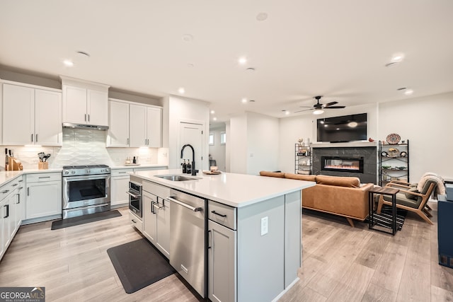 kitchen with sink, light hardwood / wood-style flooring, white cabinetry, stainless steel appliances, and an island with sink