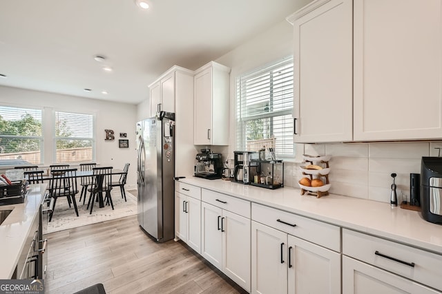 kitchen with backsplash, white cabinets, stainless steel refrigerator, and light hardwood / wood-style flooring