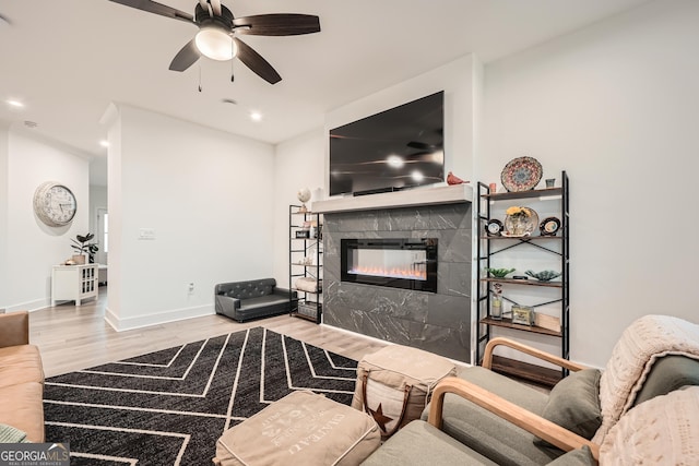 living room with a tile fireplace, ceiling fan, and light wood-type flooring