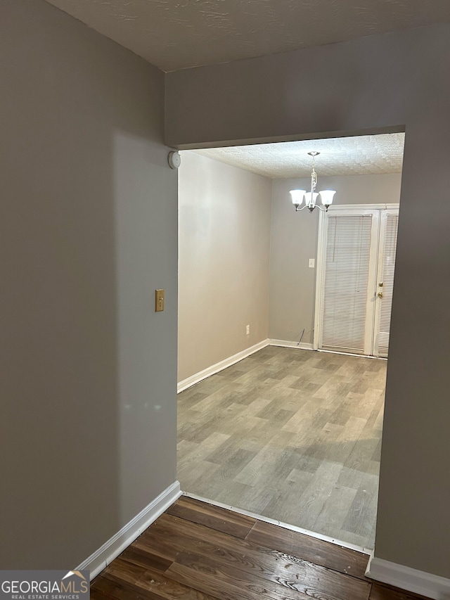 empty room featuring a textured ceiling, hardwood / wood-style flooring, and a notable chandelier