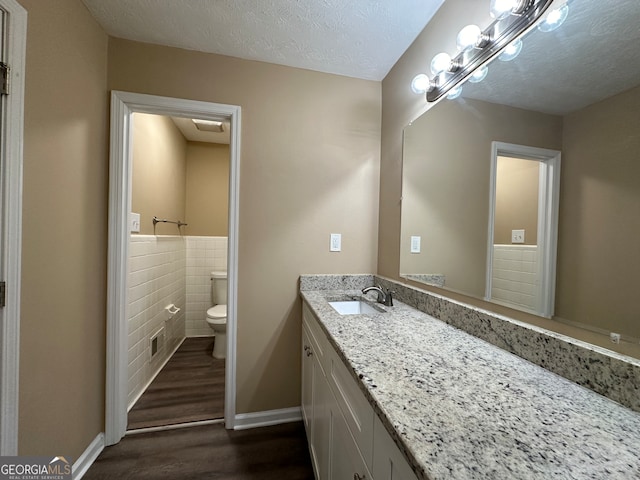 bathroom with toilet, tile walls, a textured ceiling, hardwood / wood-style flooring, and vanity