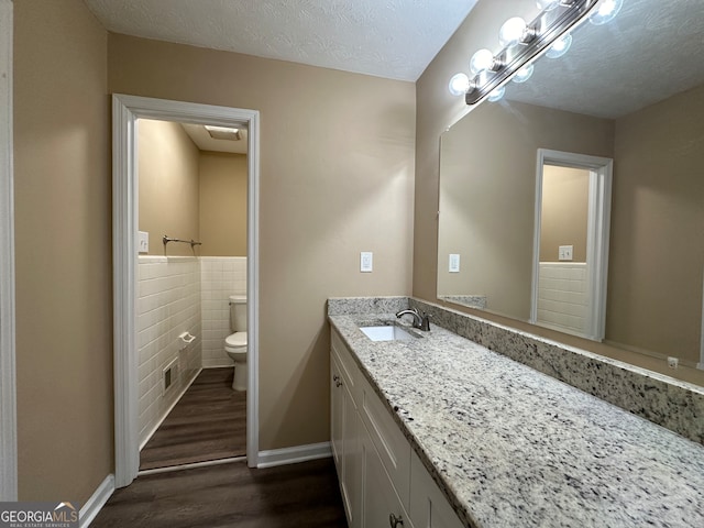 bathroom featuring toilet, tile walls, a textured ceiling, hardwood / wood-style flooring, and vanity