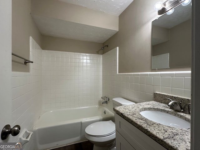 full bathroom featuring tiled shower / bath, a textured ceiling, vanity, toilet, and tile walls