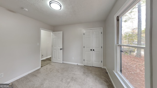 unfurnished bedroom featuring a closet, a textured ceiling, and light carpet