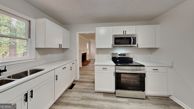 kitchen featuring stainless steel appliances, light wood-type flooring, white cabinetry, a textured ceiling, and sink