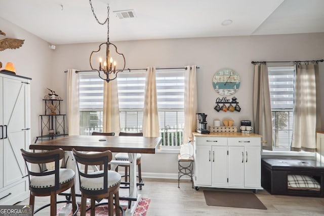 dining area with light wood-type flooring, a barn door, and a notable chandelier