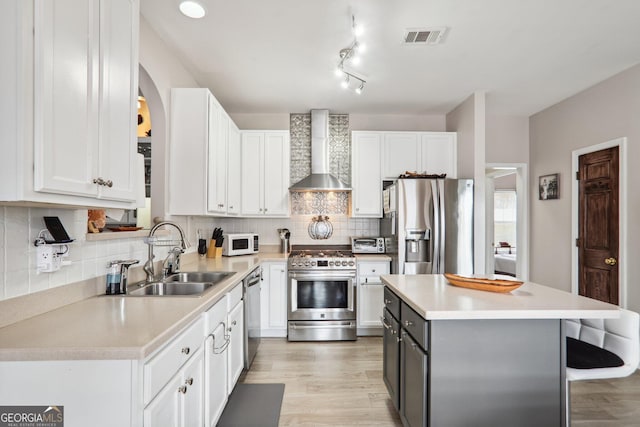 kitchen featuring white cabinetry, sink, appliances with stainless steel finishes, wall chimney exhaust hood, and light hardwood / wood-style flooring